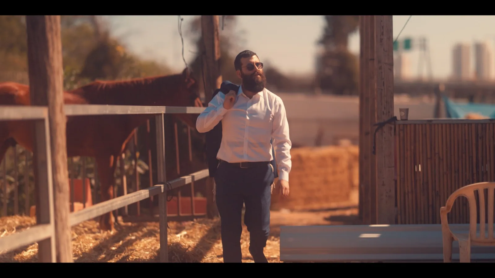 גבר בחולצה לבנה הולך לצד מכלאת סוסים באור יום
